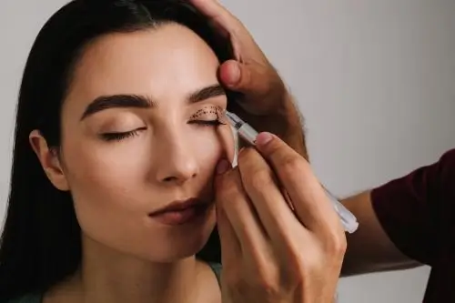 A woman having her makeup done, with her eyes closed and a makeup artist applying eyeshadow.